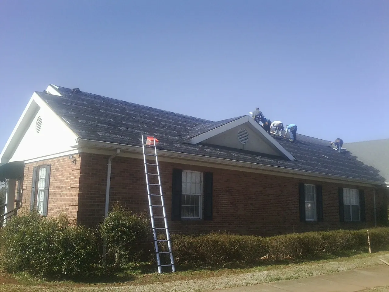 Crew tearing shingles off a brick ranch roof with a ladder set — Emergency Roof Repair work by our crew in Ringoes
