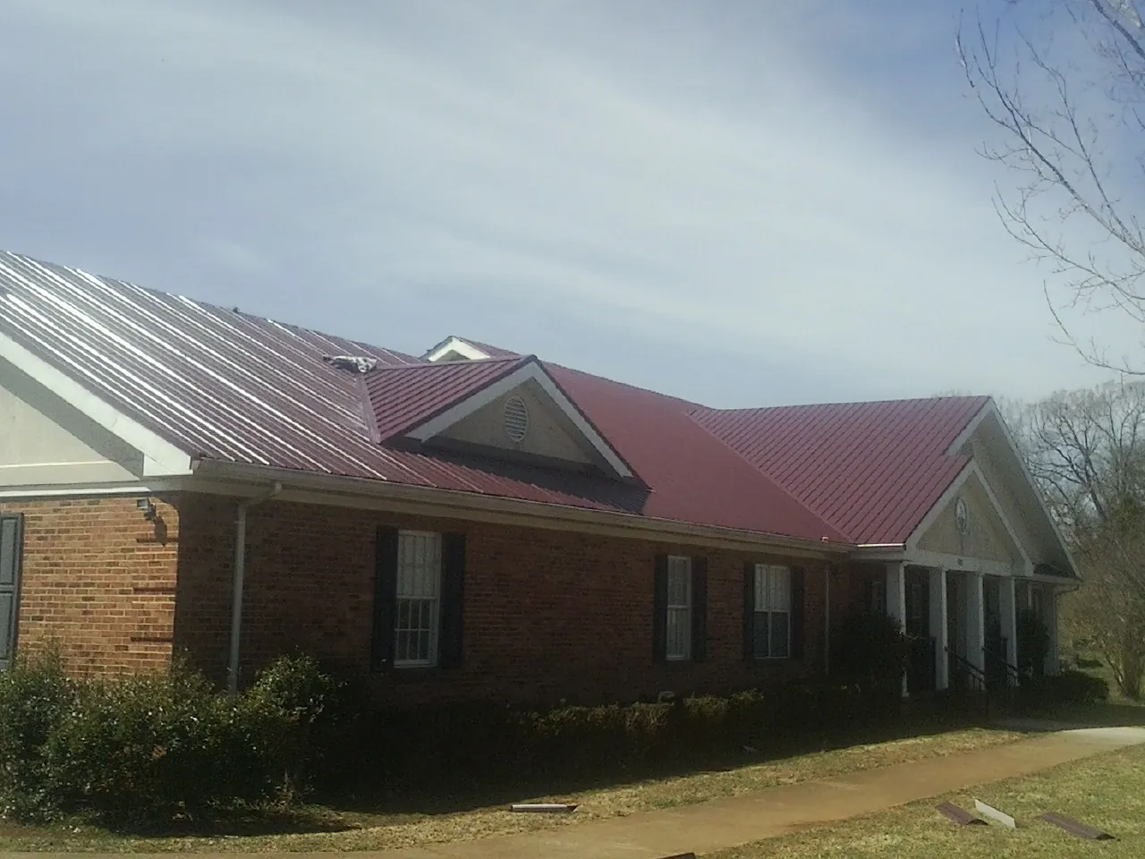 Red metal roof with gabled entries on a long brick building, from a Hail Damage Roof Repair job in Ringoes