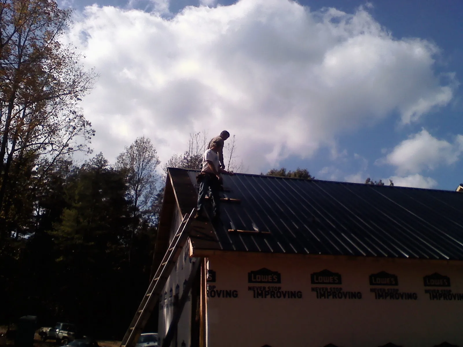 Roofer fastening dark metal panels high against a cloudy sky, from a Roof Inspection job in Ringoes